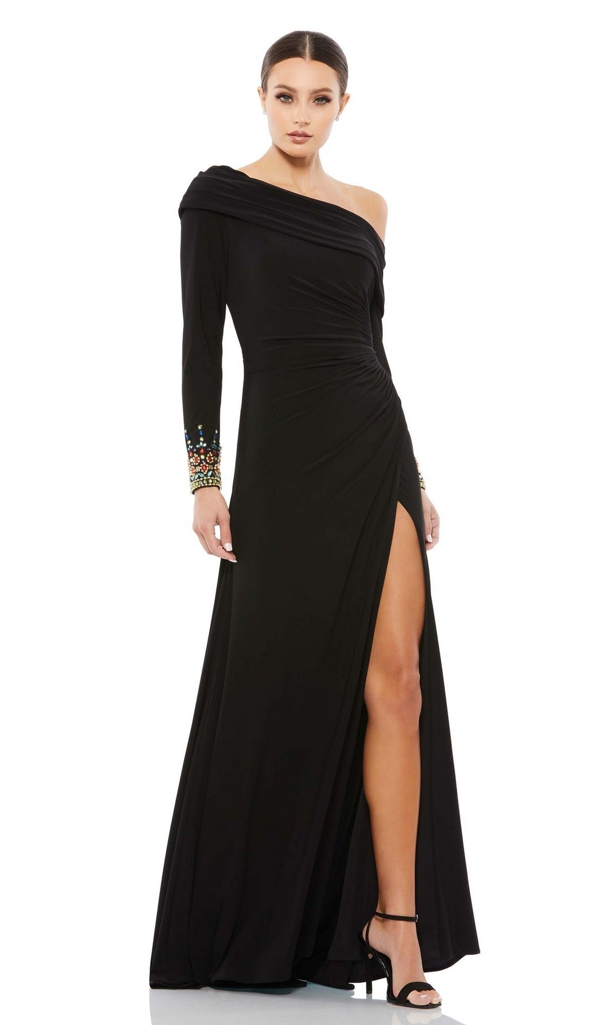 A woman models the Mac Duggal 12231 one-shoulder long formal dress—black with a thigh-high slit and beaded cuffs—paired with high heels, set against a white background.